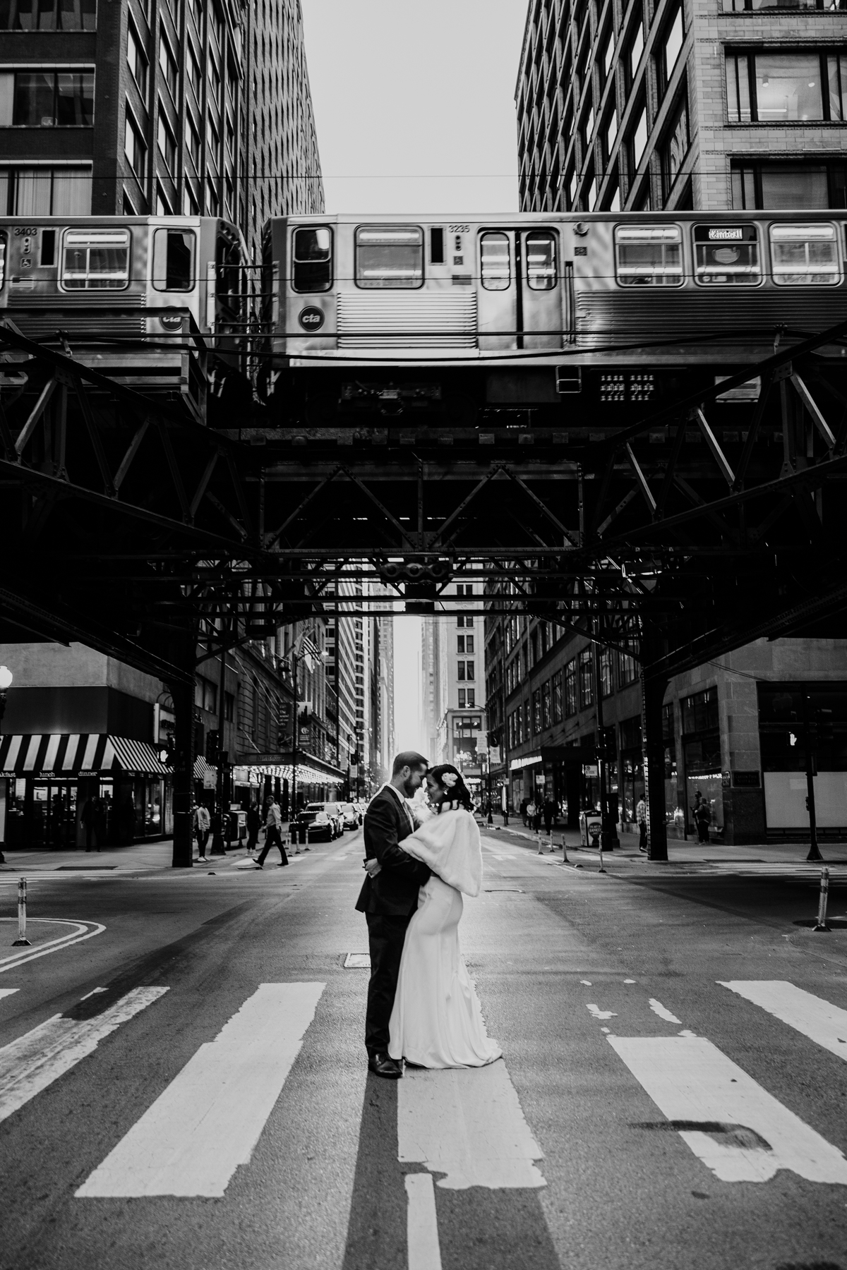 Black and white wedding photo of bride and groom in Chicago street with sunset and train going by