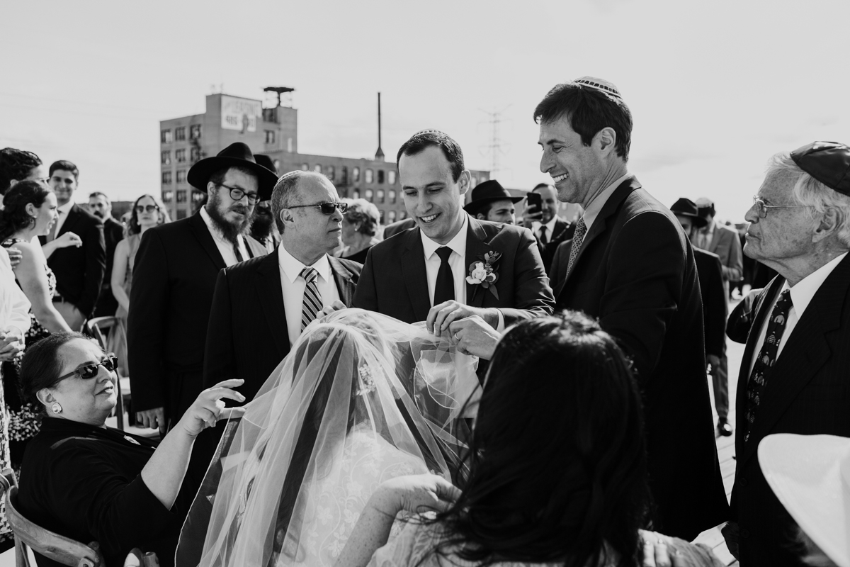 Black and white photo of groom veiling bride during Bedeken ceremony on rooftop of Ignite Glass Studio in Chicago