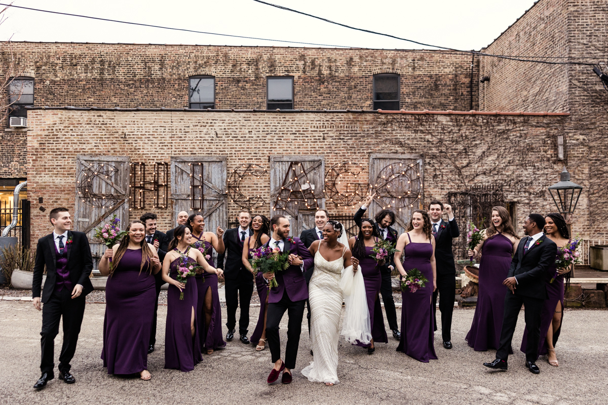 Fun photo of wedding party wearing purple walking through courtyard at Salvage One during spring wedding reception