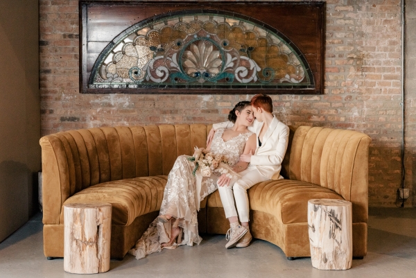 LGBTQ Couple just married on velvet yellow couch with stained glass backdrop
