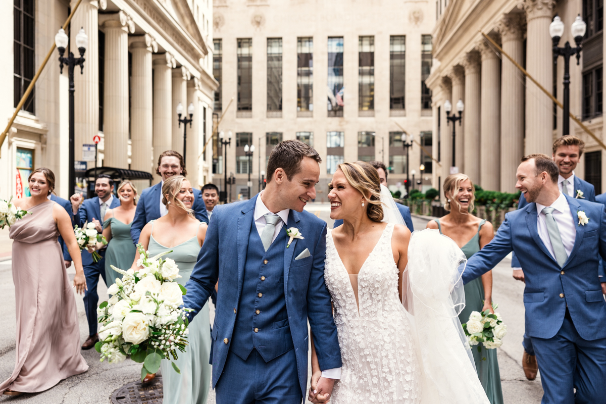 Candid wedding party photo of bride and groom walking with friends in downtown street by Chicago Board of Trade