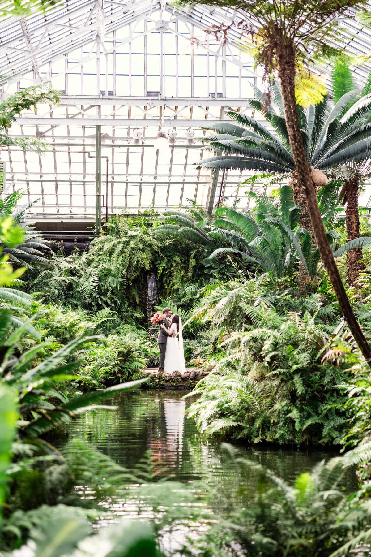 Romantic wedding photo of bride and groom surrounded by tropical greenery in Fern Room at Garfield Park Conservatory