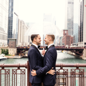 Romantic photo of two grooms under umbrella on Chicago bridge
