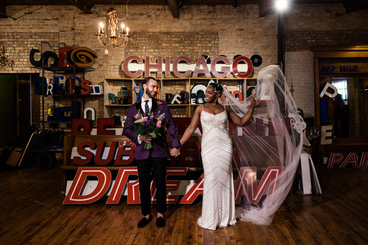 Candid photo of bride and groom with marquee letters at Salvage One wedding with flowing veil