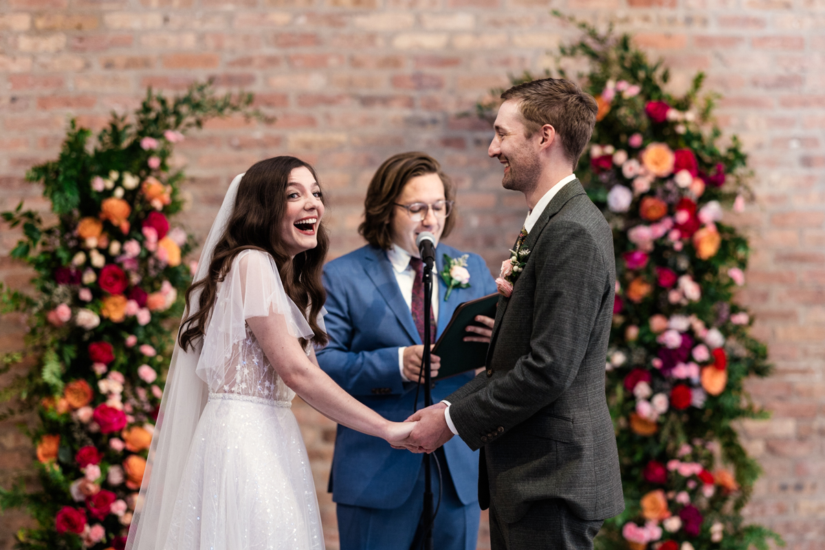 Candid photo of bride and groom laughing during wedding ceremony surrounded by colorful florals